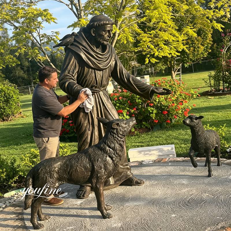 A man is maintaining an outdoor statue of Saint Francis.